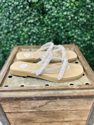 Ivory beaded flip-flop sandals with decorative straps displayed on rustic wooden crate outdoors.