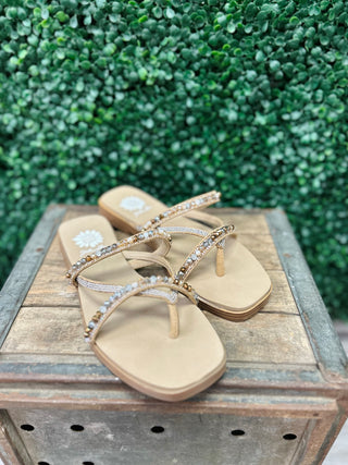 Elegant beaded flip-flop sandals with rhinestone straps displayed on rustic wooden surface outdoors.
