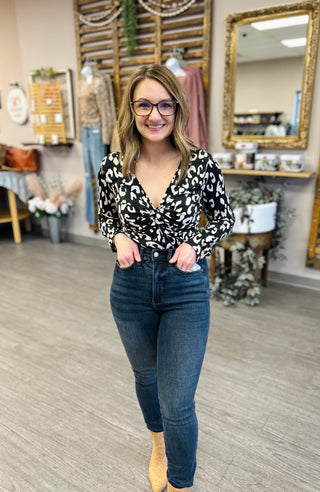 Woman wearing black leopard print twist front bodysuit with jeans in boutique setting