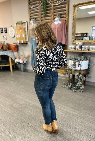 Woman wearing leopard print twist bodysuit with jeans and boots in boutique setting