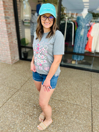Woman wearing gray floral graphic t-shirt with denim shorts and baseball cap in clothing store