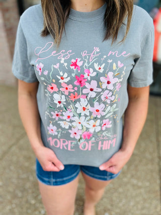 Woman wearing gray floral graphic t-shirt with "Less of Me More of Him" text and colorful flower design.