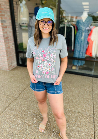 Woman wearing gray floral graphic t-shirt with denim shorts and turquoise baseball cap in retail setting