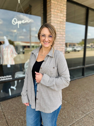 Woman smiling outdoors wearing a striped button-up shacket layered over a black top with jeans.