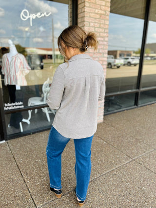 Woman wearing a striped button-up shacket with blue jeans and wedge heels, back view.