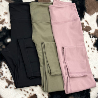 Three pairs of high-waisted compression leggings with side pockets in different colors displayed on cowhide rug.