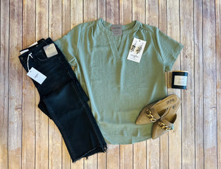 Light sage v-neck blouse styled with dark jeans, pointed flats, earrings and candle on wooden background