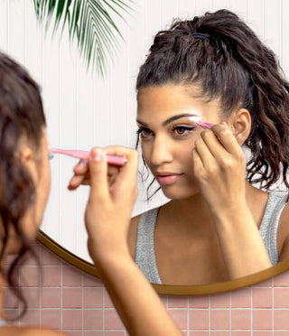Woman using illuminated tweezer for eyebrow grooming while looking in bathroom mirror