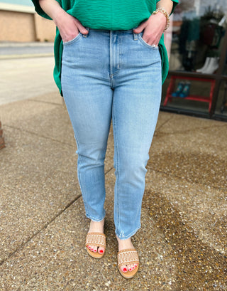 Woman wearing light wash straight leg jeans with hands in pockets, paired with sandals.