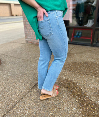Woman wearing light wash straight leg jeans with green top and brown sandals on street