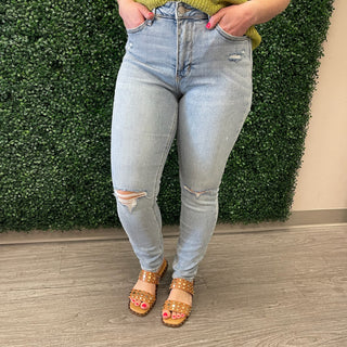 Woman wearing light wash distressed high-waisted jeans with knee rips and studded sandals.