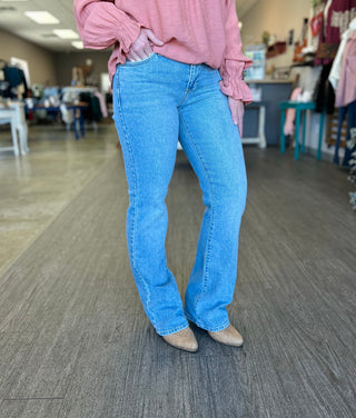 Person wearing light wash bootcut jeans with pink top and tan boots in retail store setting.