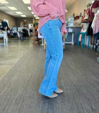 Person wearing light wash vintage slim bootcut jeans with pink top in retail store setting.