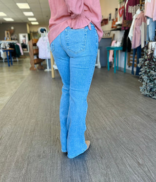 Woman wearing light wash bootcut jeans and pink top walking in clothing boutique store