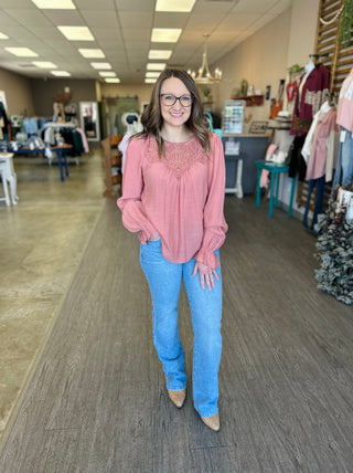 Woman wearing light wash vintage slim bootcut jeans with pink embroidered top in clothing store.