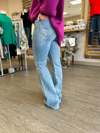 Woman wearing light blue high-rise flare jeans with purple sweater in clothing store