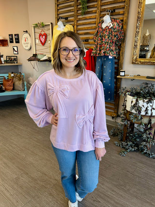 Woman wearing lilac bow-detailed pullover sweatshirt with jeans in clothing boutique store