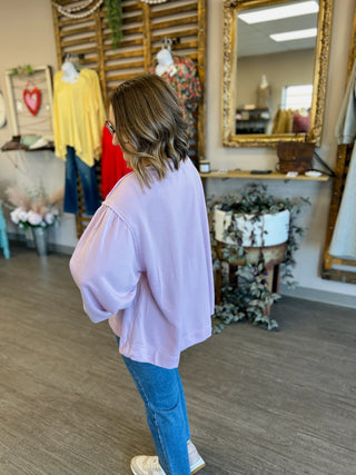 Woman wearing oversized lilac pullover with bow detail and jeans in boutique setting