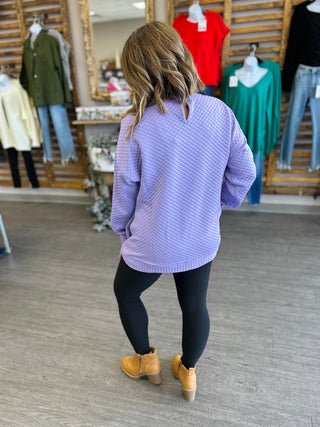 Woman wearing lilac textured top and black leggings with tan boots in clothing boutique