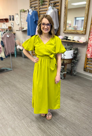 Woman wearing bright lime green wrap-style maxi dress with puffy sleeves in clothing boutique store