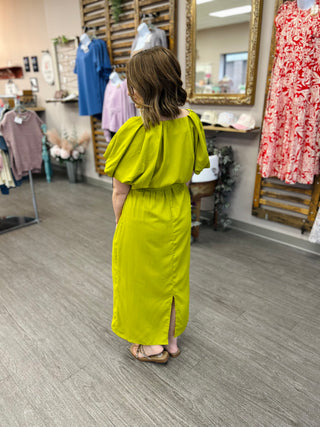Woman wearing bright yellow maxi dress with puffy sleeves and back slit in clothing store