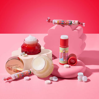 Poppy & Pout Smarties Cherry Vanilla lip balm with candy-inspired cosmetics on pink surface