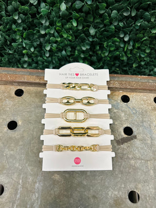 Set of five gold-toned chain hair tie bracelets on white display card against wooden surface.