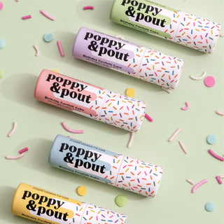 Colorful Poppy & Pout Birthday Confetti Cake lip balm tubes scattered with sprinkles on light background