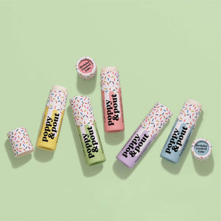 Colorful lip balm tubes with sprinkle pattern packaging arranged on green background with round containers.