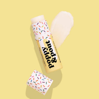 Poppy & Pout lip balm with colorful sprinkle design on yellow background, cap removed showing product.