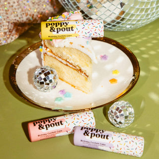 Poppy & Pout Birthday Confetti Cake lip balm tubes displayed with cake slice and disco balls on festive background.