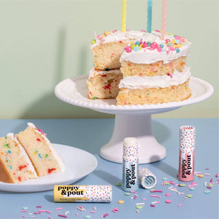 Colorful birthday confetti cake with candles displayed alongside Poppy & Pout lip balm tubes and scattered sprinkles.