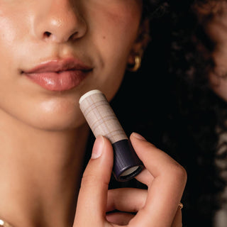 Woman holding Poppy & Pout lip balm tube with plaid packaging near her glossy lips