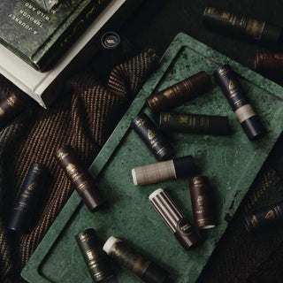 Lip balm tubes arranged on green surface with books and textured fabric in background