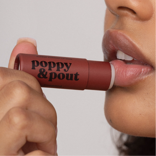 Person applying Poppy & Pout lip balm to lips, showing product packaging and application.