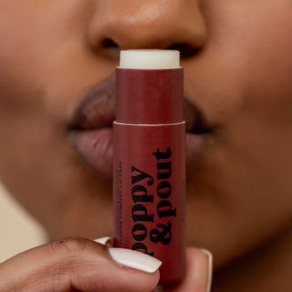 Person holding Poppy & Pout Cinnamint lip balm tube near their lips, showcasing the product packaging.