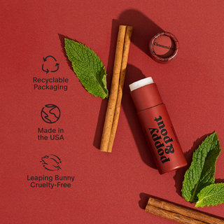 Poppy & Pout Cinnamint lip balm with cinnamon sticks and mint leaves on red background showcasing sustainable features.