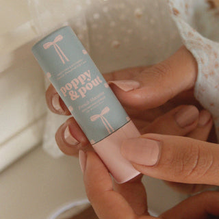 Hands holding Poppy & Pout French Macaron lip balm tube with mint green packaging and pink bow design.