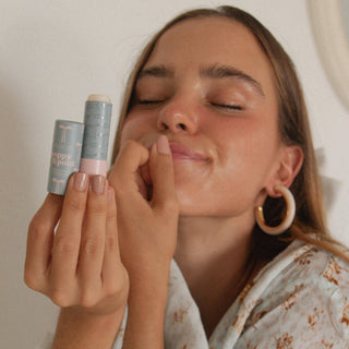 Woman with eyes closed holding Poppy & Pout lip balm, demonstrating smooth application on lips.