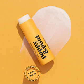 Yellow Poppy & Pout lip balm tube with white cap on orange background with heart-shaped sponge