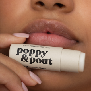 Person holding Poppy & Pout lip balm near glossy lips with white nail polish