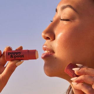 Woman applying Poppy & Pout lip balm outdoors in natural sunlight with eyes closed peacefully.