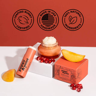 Poppy & Pout lip balm tube with jar of scrub, orange box, and fresh fruit on white surface.