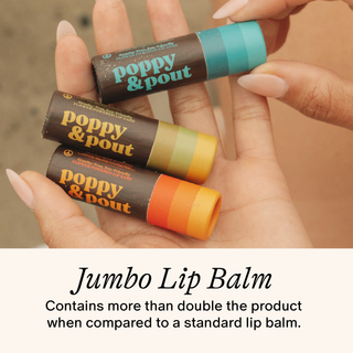 Hand holding three Poppy & Pout jumbo lip balm tubes in different colors against neutral background.