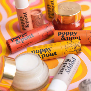 Poppy & Pout lip balm tubes and tins arranged on colorful retro background with poppy flower designs.