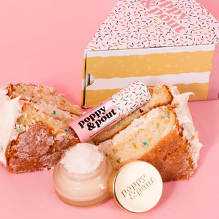 Birthday cake slices with colorful sprinkles alongside Poppy & Pout lip balm and lip scrub products on pink background.