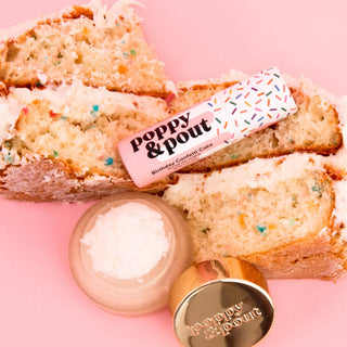 Birthday confetti cake flavored lip balm tubes with colorful sprinkle design on pink background with cake slices.