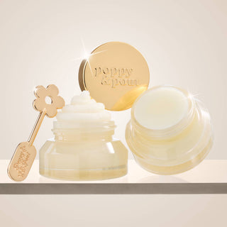 Poppy & Pout lip scrub and balm jars open beside gold daisy applicator wand.