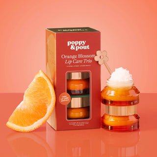 Poppy & Pout Lip Care Trio gift set box beside stacked lip scrub and mask jars with orange slice.