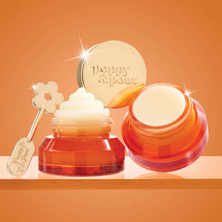 Poppy & Pout lip balm jars open displaying creamy product with gold applicator spoon on orange background.